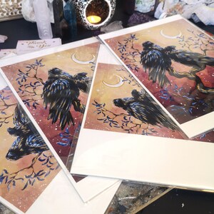 May include: Three watercolor prints featuring black birds perched on branches with crescent moons in the background. The prints have a soft, dreamy aesthetic with a light pink and blue color scheme.