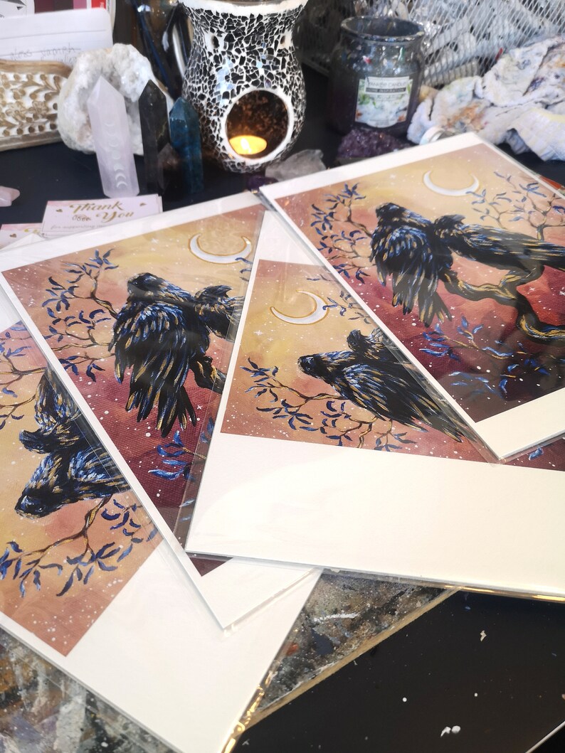 May include: Three watercolor prints featuring black birds perched on branches with crescent moons in the background. The prints have a soft, dreamy aesthetic with a light pink and blue color scheme.