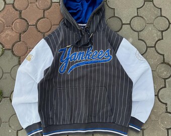 May include: A gray and white pinstripe hoodie with the word "Yankees" in blue script across the chest. The hoodie has a blue interior, white sleeves, and a front pocket. The bottom hem and cuffs have blue and white stripes.