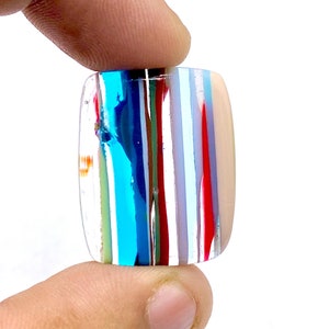 May include: A rectangular glass tile with a colorful striped pattern. The tile has a variety of colors, including blue, red, white, and green. The tile is translucent and has a glossy finish.