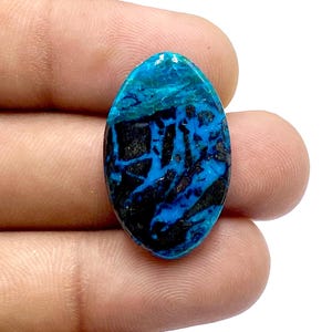 Op de afbeelding: Ovaalvormige cabochon edelsteen met een blauw en zwart patroon. De edelsteen heeft een glad, gepolijst oppervlak.