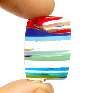 May include: A colorful glass cabochon with a striped pattern in shades of red, blue, green, and white.