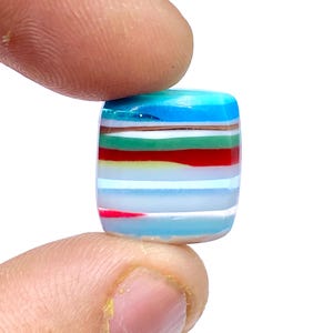 May include: A rectangular, multi-colored gemstone with alternating layers of blue, green, red, white, and yellow. The gemstone is smooth and polished.