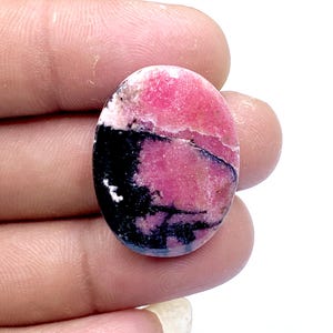 May include: Oval-shaped gemstone with a striking color pattern. The stone features a blend of vibrant pink, black, and white hues. The pink dominates the upper portion, transitioning to black and white at the base. A unique piece for jewelry.