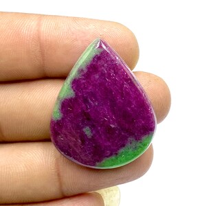 May include: A teardrop-shaped green and pink gemstone cabochon. The stone has a mottled pattern of green and pink.