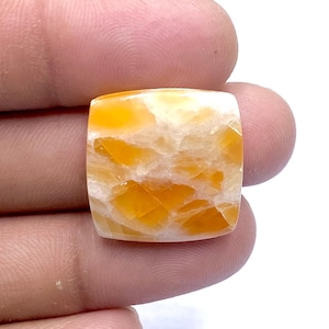 May include: A square-shaped, orange and white gemstone cabochon with a marbled pattern.