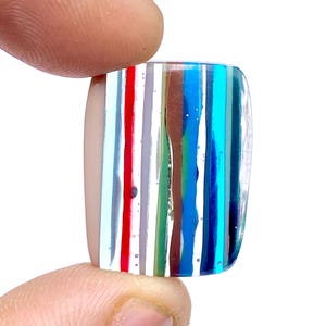 May include: A rectangular piece of fused glass with a layered, striped pattern in shades of blue, green, red, white, and brown.
