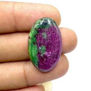 Könnte beinhalten: Ovaler grüner und violetter Edelstein mit einer glatten, polierten Oberfläche.
