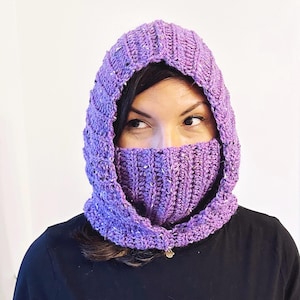 May include: A purple crocheted hooded cowl with a ribbed texture. The cowl is worn by a person, covering their head and neck.