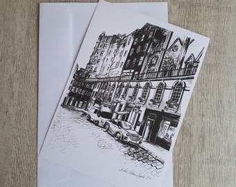 Puede incluir: Dibujo a tinta en blanco y negro de una escena callejera con edificios, coches y adoquines. La obra de arte está en una tarjeta blanca con un sobre a juego. La firma del artista y el año 2020 son visibles.