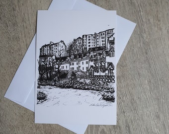 Puede incluir: Un dibujo a tinta en blanco y negro de un paisaje urbano europeo, con edificios a orillas de un río. La obra de arte está en una tarjeta blanca, con un sobre blanco detrás. El dibujo está firmado en la esquina inferior derecha.