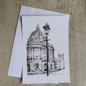 Peut inclure: Dessin à l'encre noir et blanc d'un bâtiment à dôme avec un lampadaire au premier plan. Le dessin est sur une carte blanche avec une enveloppe assortie. La carte est signée "E. de la Calera Sydenham '21".
