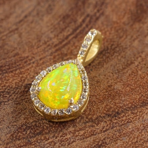 Puede incluir: Un colgante de ópalo amarillo en forma de lágrima con un halo de piedras de circonita cúbica transparentes engastadas en oro.