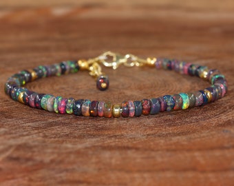 May include: A delicate bracelet made with small, iridescent black opal beads. The bracelet has a gold clasp and extender chain.