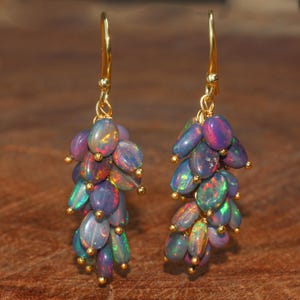 May include: A pair of gold-toned earrings featuring clusters of oval-shaped opals. The opals display a range of colors, including blue, purple, green, and red, with a shimmering, iridescent effect. The earrings have a hook closure.