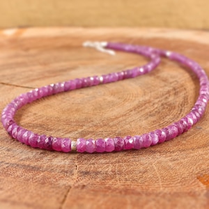 May include: A pink gemstone necklace with silver beads. The necklace is made of faceted pink gemstones and silver beads. The necklace is on a wooden surface.