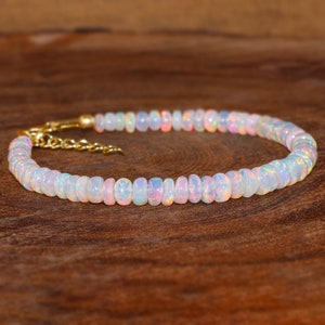 May include: A delicate white opal beaded bracelet with a gold clasp. The bracelet is made of small, round beads that are strung together on a thin gold chain.