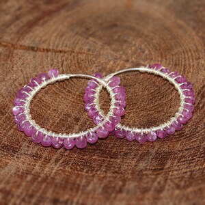Peut inclure: Une paire de boucles d'oreilles créoles en argent avec des pierres précieuses roses. Les boucles d'oreilles sont faites de fil et ont un aspect délicat et féminin.