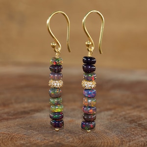 May include: A pair of gold earrings with a dangling chain of iridescent black opal beads and a small row of clear cubic zirconia stones.