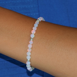 May include: A white opal beaded bracelet with silver accents. The bracelet is on a person's wrist.