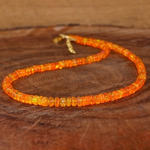 Puede incluir: Un collar hecho de cuentas de ópalo naranja. Las cuentas son pequeñas y redondas, y están enhebradas en una cadena de oro.