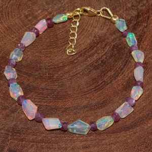 May include: A delicate bracelet made with iridescent white opal and purple gemstone beads. The bracelet has a gold clasp.