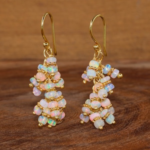 Könnte beinhalten: Ein Paar goldene Ohrhänger mit mehreren kleinen weißen Opalperlen. Die Ohrringe sind aus Golddraht gefertigt und haben eine Tropfenform.