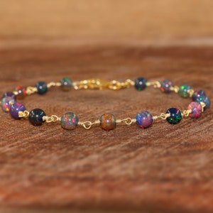 May include: A bracelet with black opal beads, each displaying flashes of colour, strung on gold-coloured wire. The bracelet is secured with a gold-coloured clasp. The beads are approximately 0.6 cm in diameter, showcasing a piece of fine jewellery.