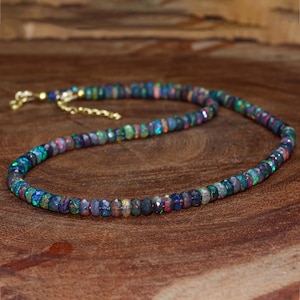 May include: A black opal gemstone necklace with a gold chain clasp. The necklace is made of small, round beads that are strung together.