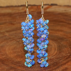 Puede incluir: Un par de pendientes largos y colgantes con una cascada de cuentas de ópalo azul. Los pendientes están hechos de oro y presentan un diseño delicado en forma de lágrima.