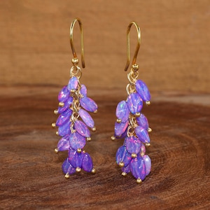 May include: A pair of gold dangle earrings featuring a cluster of purple opal beads. The earrings are long and delicate, with a cascading design.