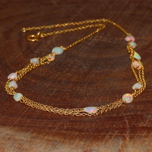 Puede incluir: Un collar de cadena de oro con múltiples hebras y piedras de ópalo blanco. El collar está sobre una superficie de madera marrón.