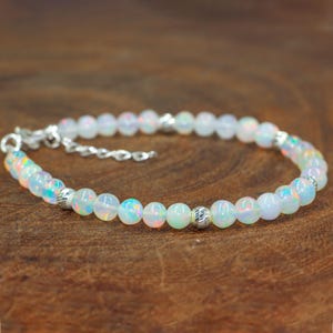 May include: A delicate white opal beaded bracelet with silver accents. The bracelet is made with small, round opal beads and features two silver bead accents.