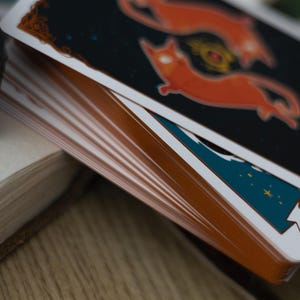 May include: A deck of cards with a blue and orange design. The top card features a stylized illustration of two orange cats with a star-filled night sky background. The card text reads "Change is Coming".