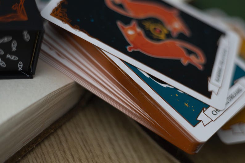 May include: A deck of cards with a blue and orange design. The top card features a stylized illustration of two orange cats with a star-filled night sky background. The card text reads "Change is Coming".
