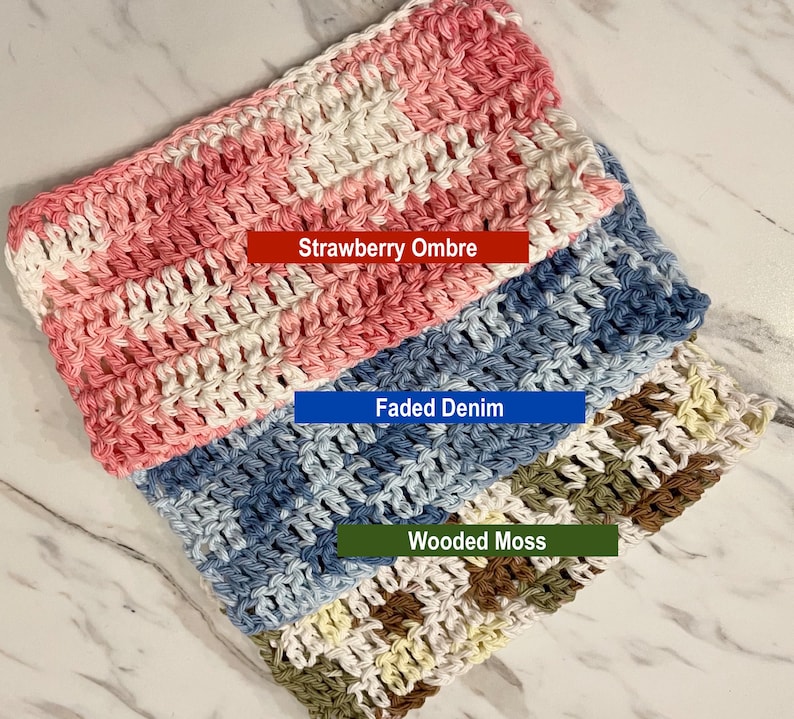 May include: Three rectangular crochet washcloths featuring variegated yarn patterns. The top cloth is pink and white labeled Strawberry Ombre, the middle is blue and white labeled Faded Denim, and the bottom is green, brown, and white labeled Wooded Moss.