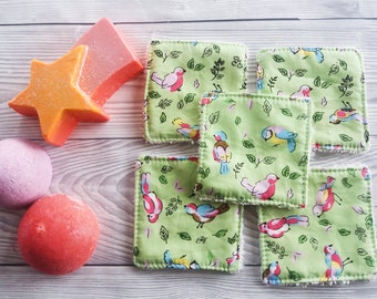 May include: Six green fabric squares with a white border and a repeating pattern of colorful birds and leaves. Two pink bath bombs and a star-shaped orange bath bomb are also in the image.