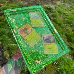 May include: A green resin tray with gold glitter and three Pokemon cards. The cards are for Venusaur, Ivysaur, and Bulbasaur.