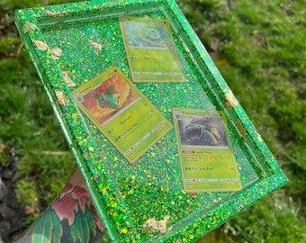 May include: A green resin tray with gold glitter and three Pokemon cards. The cards are for Venusaur, Ivysaur, and Bulbasaur.
