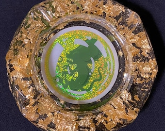 May include: A glass ashtray with a gold leaf design and a green monster graphic in the center.