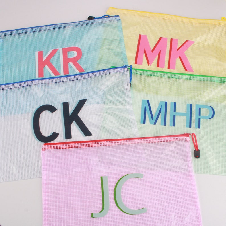May include: A collection of colorful mesh zipper pouches. Each pouch features a different set of initials in bold, contrasting colors. The pouches are in shades of blue, yellow, pink, and green, with red, blue, and green zippers.