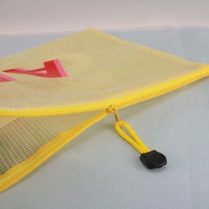 May include: A yellow mesh zipper pouch with a yellow zipper and pull. The pouch has a red and pink design on the front. The zipper pull is yellow with a black plastic end.