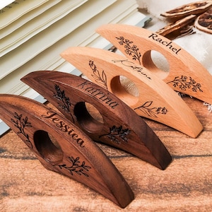 May include: Four wooden thumb page holders with names engraved: Jessica, Katrina, Rachel, and Katrina. Each holder has a circular opening and is decorated with floral designs. The wood tones vary from light to dark brown.