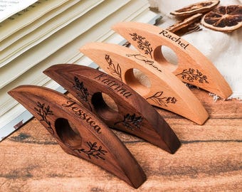 May include: Four wooden thumb page holders with names engraved: Jessica, Katrina, Rachel, and Katrina. Each holder has a circular opening and is decorated with floral designs. The wood tones vary from light to dark brown.