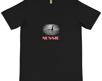 May include: Black t-shirt with a graphic of the Loch Ness Monster in a black and white photo with the word "NESSIE" in pink letters below the image.