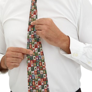 May include: A patterned tie featuring a repeating Christmas-themed design. The tie has a dark green background with small squares containing images of gingerbread men, snowmen, and Christmas trees. The tie is being adjusted by a person wearing a white dress shirt.