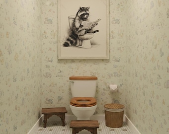 May include: A whimsical bathroom scene featuring a framed black and white illustration of a raccoon reading on a toilet. The room has light green wallpaper with a repeating pattern, a wooden toilet seat, and small wooden step stools.