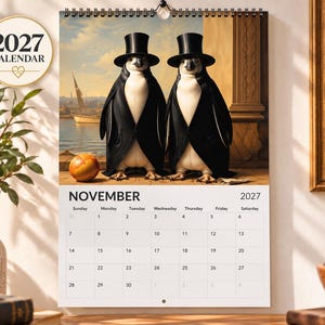 Peut inclure: Un calendrier mural 2027 affichant la page de novembre avec une illustration surréaliste de deux manchots portant des hauts-de-forme noirs et des queues-de-pie, debout sur une terrasse en pierre près d'un plan d'eau avec un voilier.
