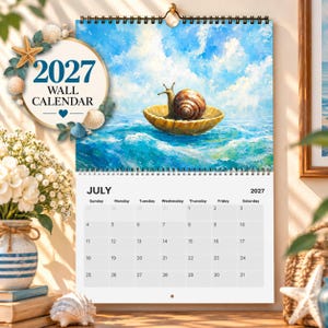 Peut inclure: Un calendrier mural 2027 avec une reliure à spirale. La partie supérieure présente une peinture à l'huile représentant un escargot dans un coquillage flottant sur des vagues bleues. La partie inférieure affiche la grille du mois de juillet 2027.