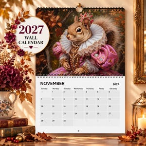 Peut inclure: Un calendrier mural 2027 représentant un écureuil vêtu d'une tenue royale rose ornée avec un col à volants blanc et des bijoux en perles. La page du calendrier affiche le mois de novembre 2027 avec une grille de dates et le texte 2027 WALL CALENDAR.